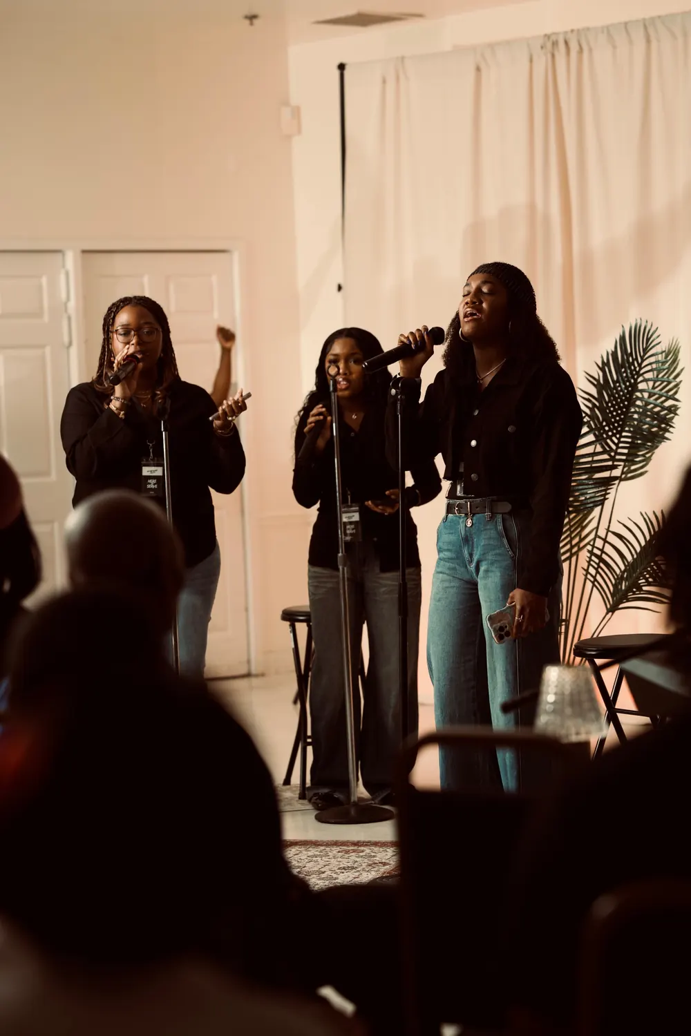 Three worship leaders singing together in a softly lit room while the congregation listens