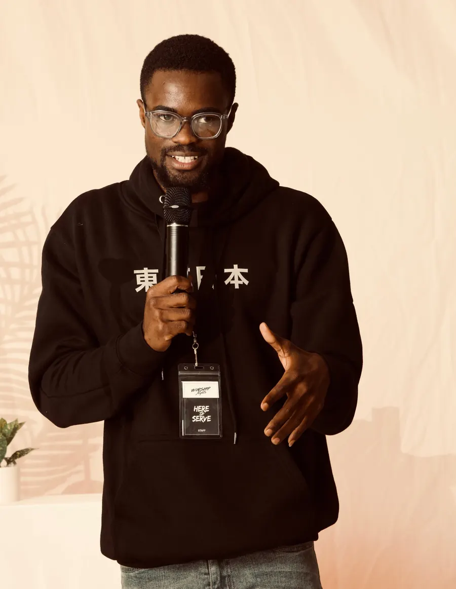 A smiling man in a black hoodie speaking into a microphone