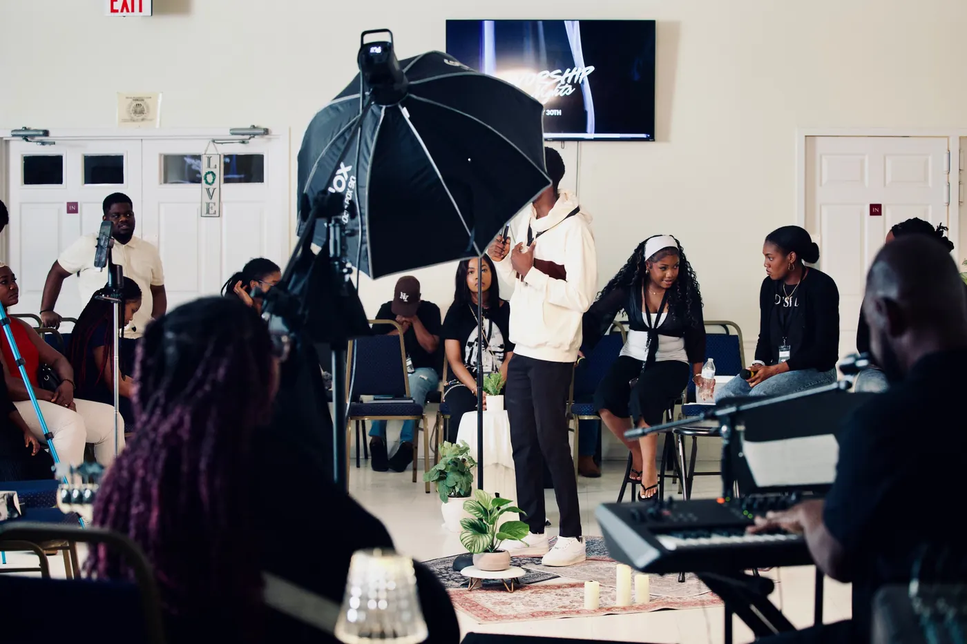 A circle of people gathered for worship in a bright hall, with a keyboardist in the foreground