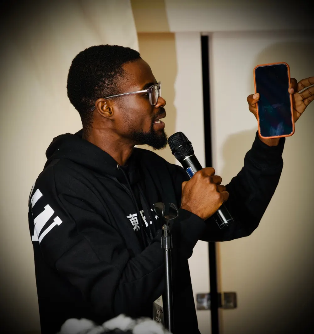 A man speaking into a microphone and holding up a phone