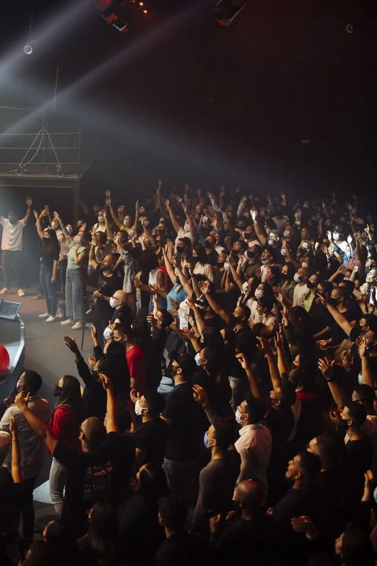 A large crowd worshiping with hands raised under stage lights