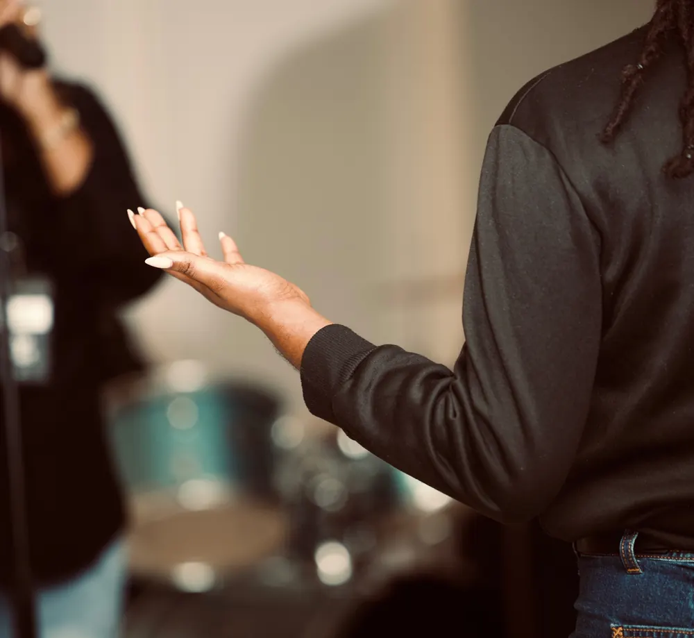 An open hand extended toward a singer in a blurred worship room