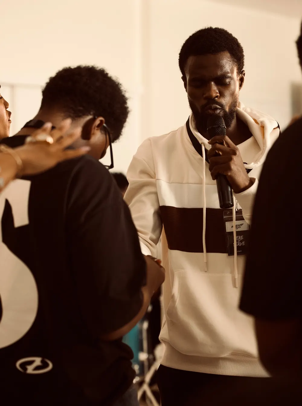 A man praying with a microphone while others gather close around him