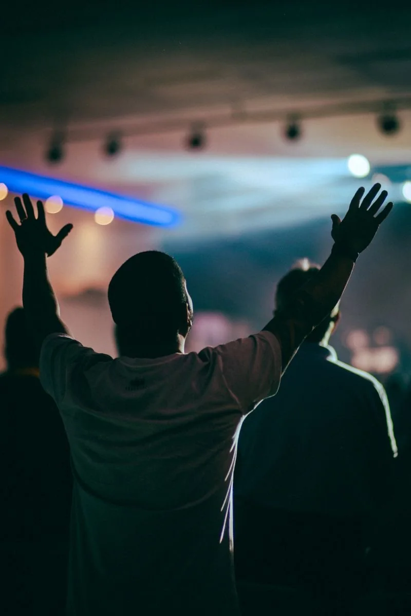 A person worshiping with both hands raised toward stage lights